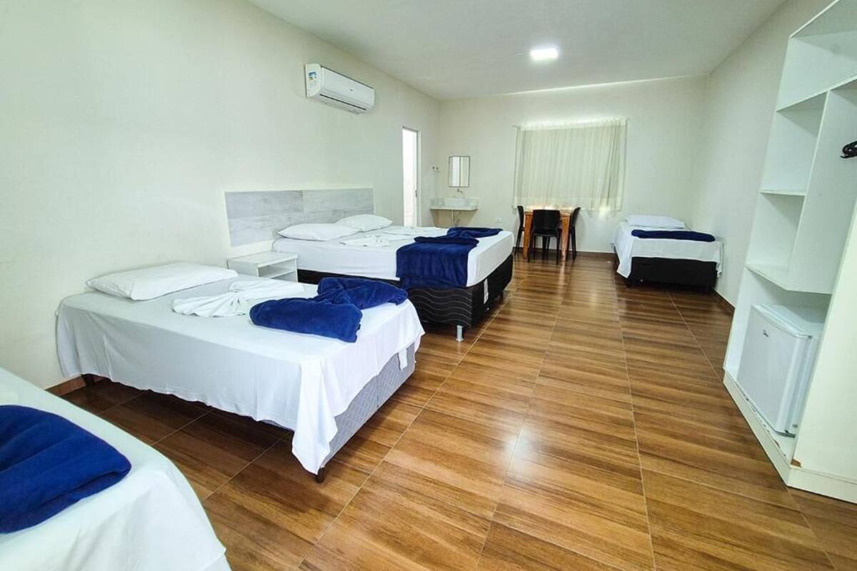 A hotel room with two beds, a desk, a chair, and a white wardrobe.