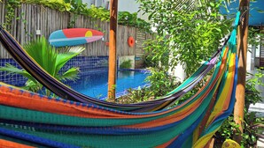 A hammock in a backyard with a pool, surrounded by greenery and a wooden fence. - Maresia Unique (Ipojuca)