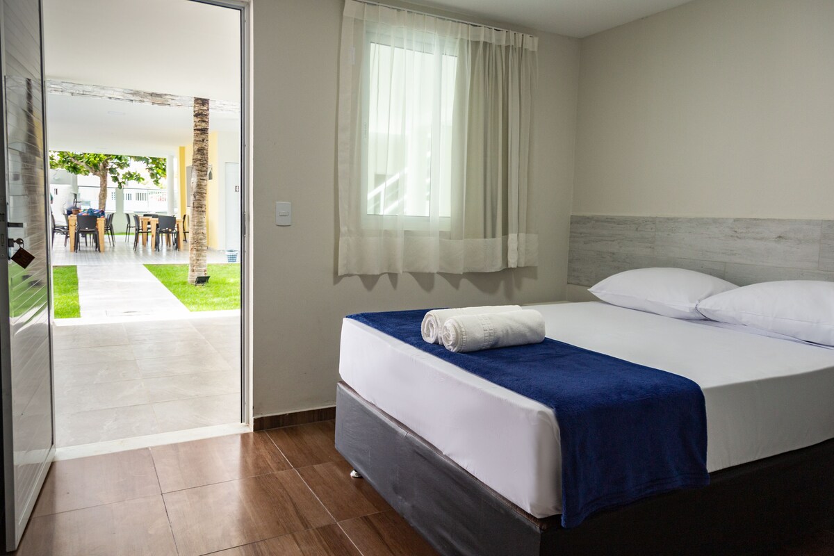 A hotel room with a bed, a window with sheer curtains, and a view of the outdoor area.