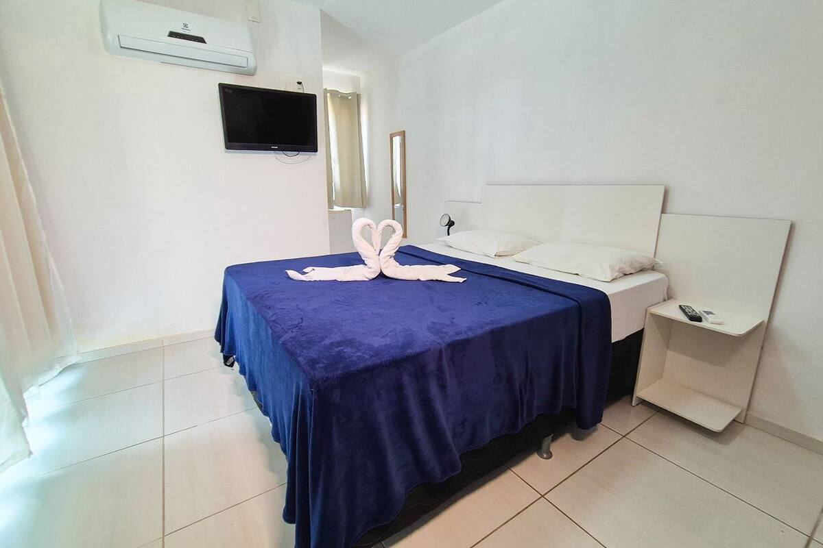 A hotel room with a bed, a bedside table, a mirror, and a wall-mounted TV.