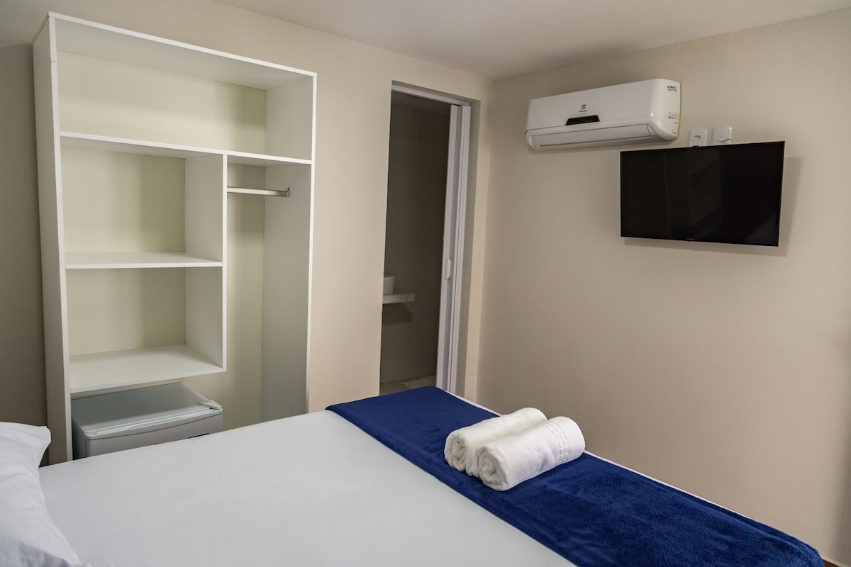 A hotel room with a bed, a wardrobe, a television, and an air conditioning unit.