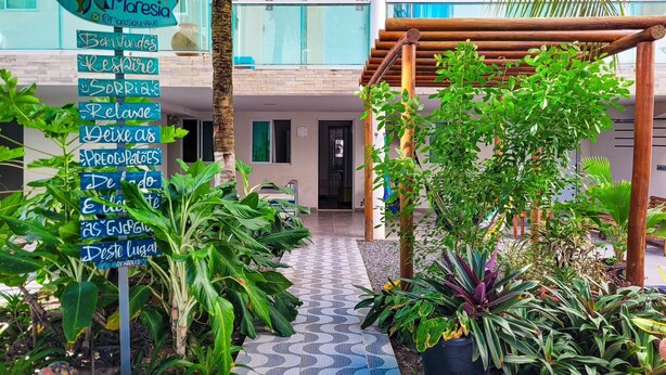 A hotel entrance with a signboard displaying various amenities and a covered outdoor area with plants. - Maresia Unique (Ipojuca)