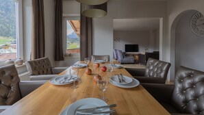 Comedor con una mesa de madera dispuesta para cuatro personas, rodeado de sillas de cuero, y vista a las montañas a través del ventanal.