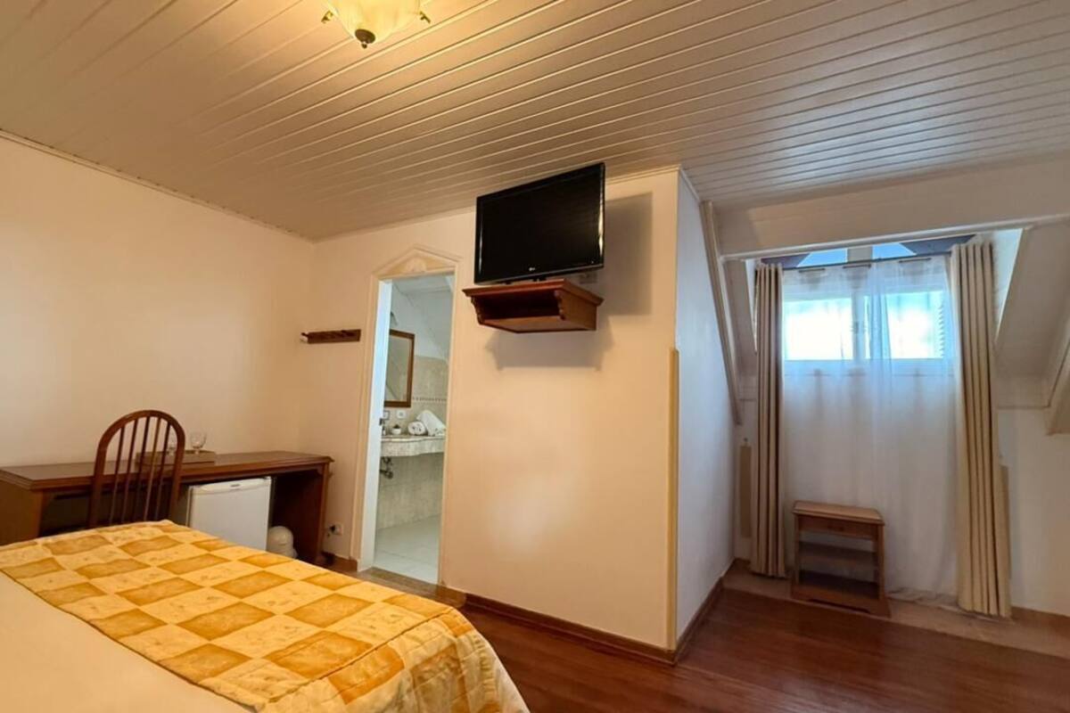 Een slaapkamer met een bed, een bureau, een televisie, een spiegel en een raam met gordijnen.