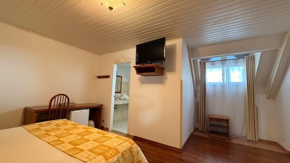 A bedroom with a bed, a desk, a television, a mirror, and a window with curtains. - Pousada Dom Alfredo José (Campos do Jordão)