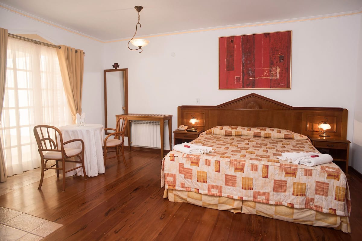 Een hotelkamer met een houten bed, een bureau met stoel, een tafel met stoelen en een grote spiegel aan de muur.