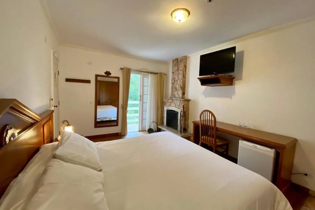 Een hotelkamer met een bed, een bureau, een televisie, een open haard en een deur naar een balkon.