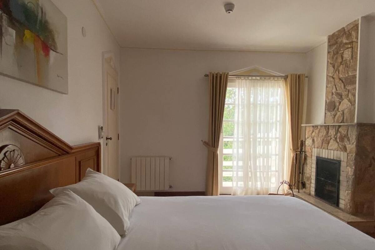 Een slaapkamer met een groot bed, een open haard en uitzicht door een raam met gordijnen.