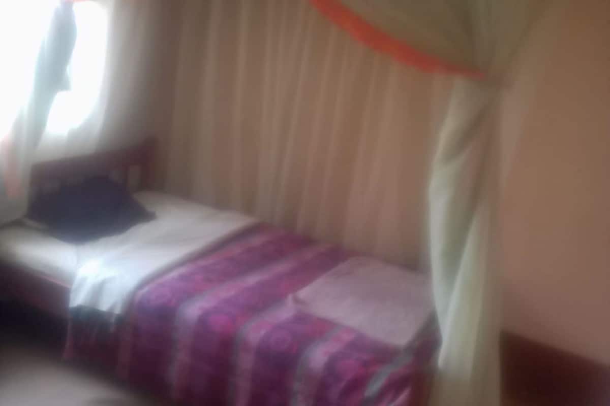 Una habitación con cama, ventana con cortinas y una colcha.
