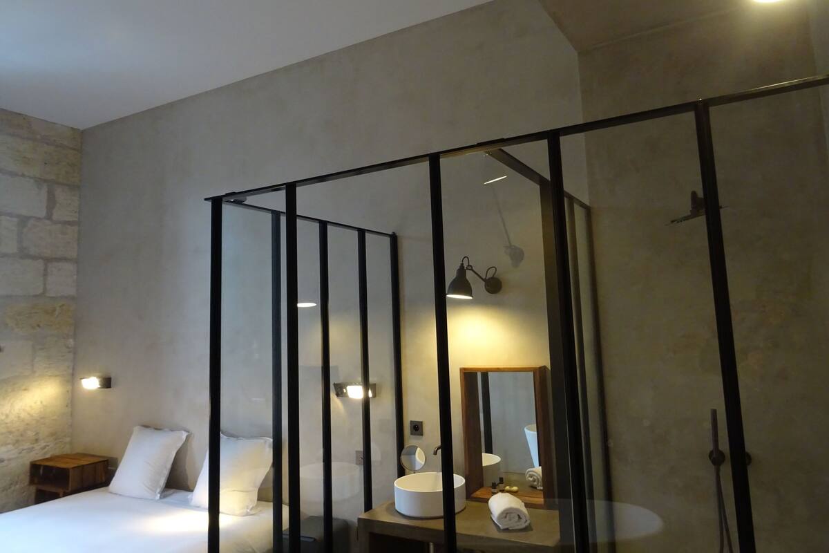 Een moderne slaapkamer met een bed, nachtkastje en een badkamer met wastafel en spiegel.