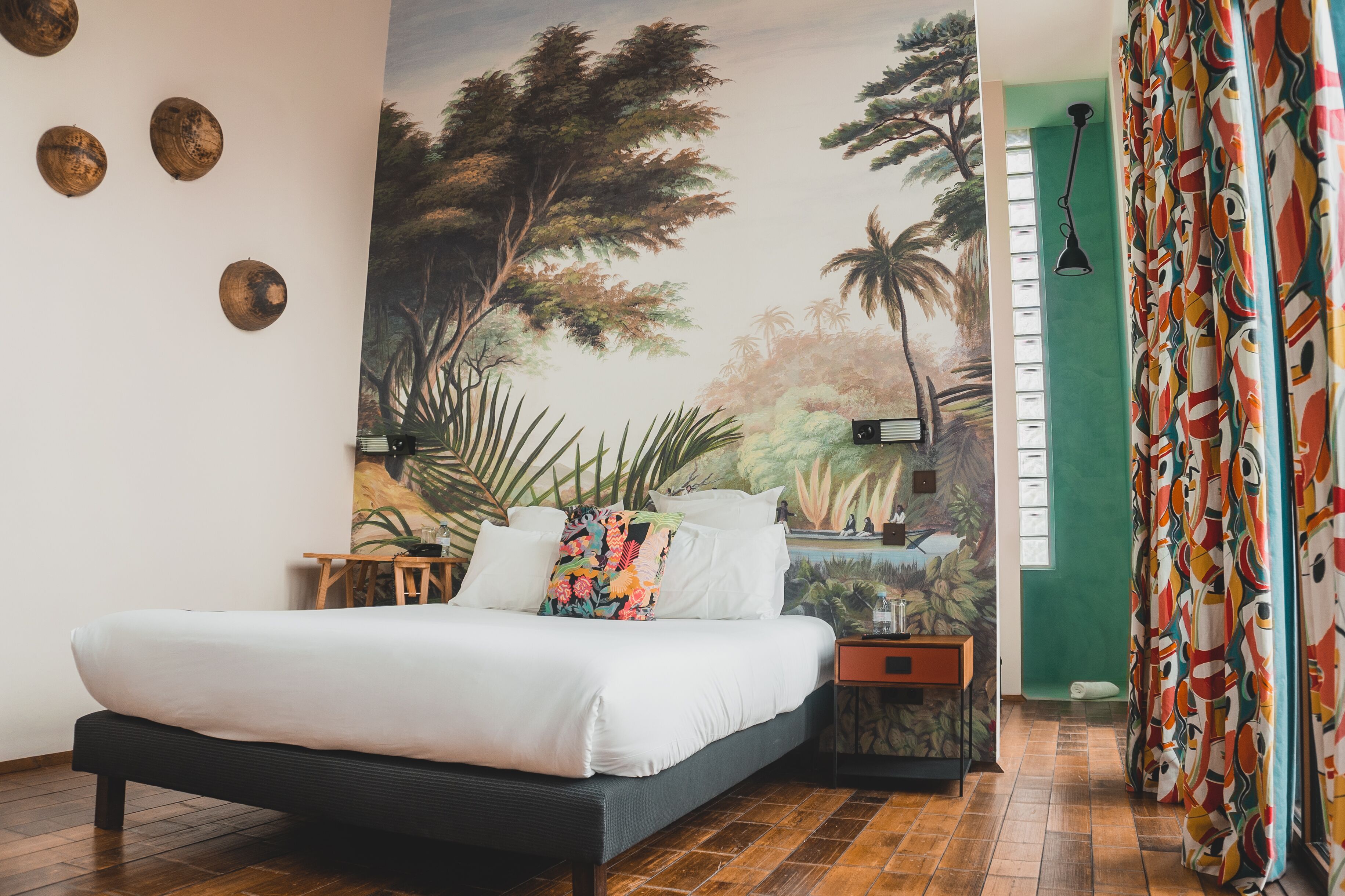 Un dormitorio con una cama, una mesita de noche, un mural en la pared y una cortina.