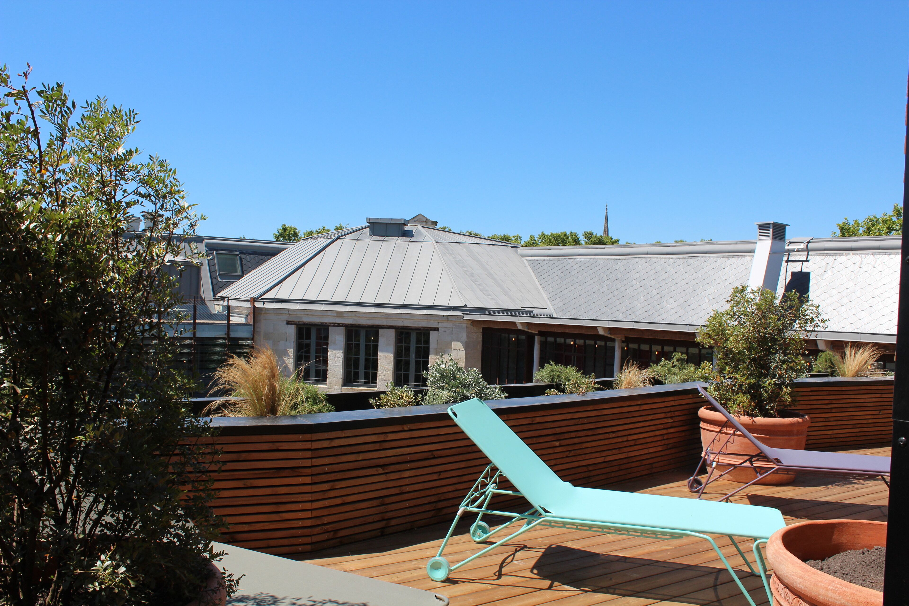 Um terraço no telhado com uma cadeira de lounge, vasos de terracota e vista para um edifício moderno.