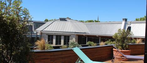 A rooftop patio with a lounge chair, terracotta planters, and a view of a modern building.