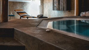 Área de piscina interior moderna con vista despejada, una silla de descanso y una pequeña mesa con una botella.