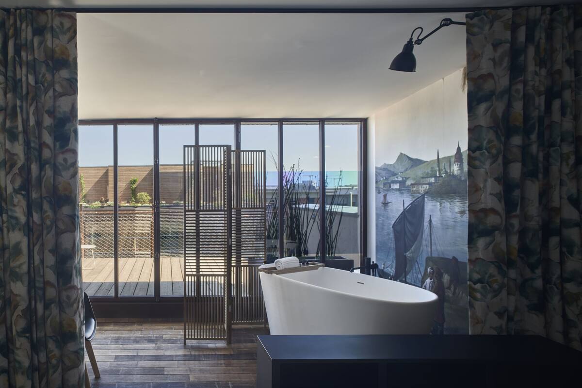 Een moderne badkamer met een vrijstaand bad, grote ramen en uitzicht op een kustlandschap.