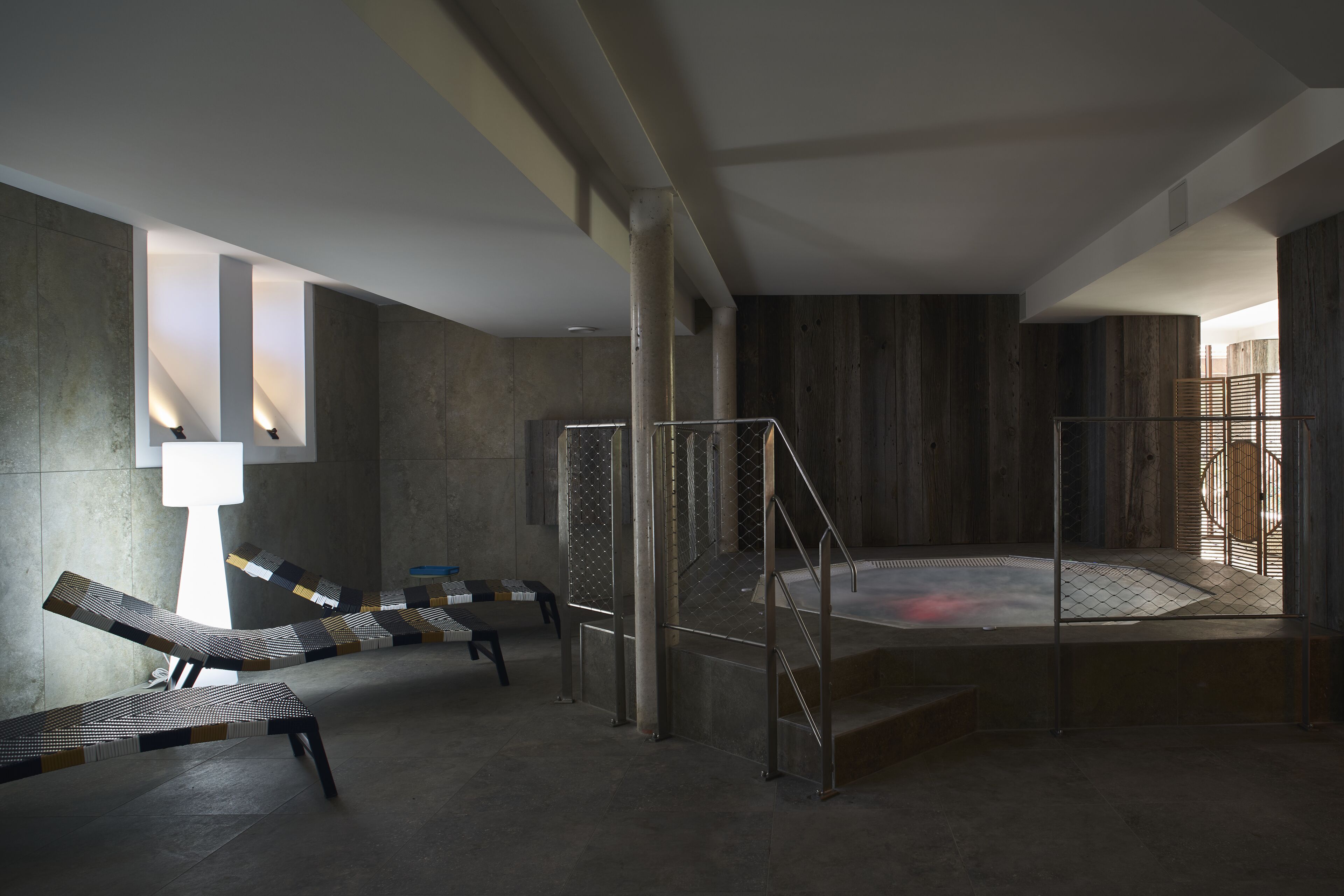 A modern spa with a hot tub, lounge chairs, and a stone wall.