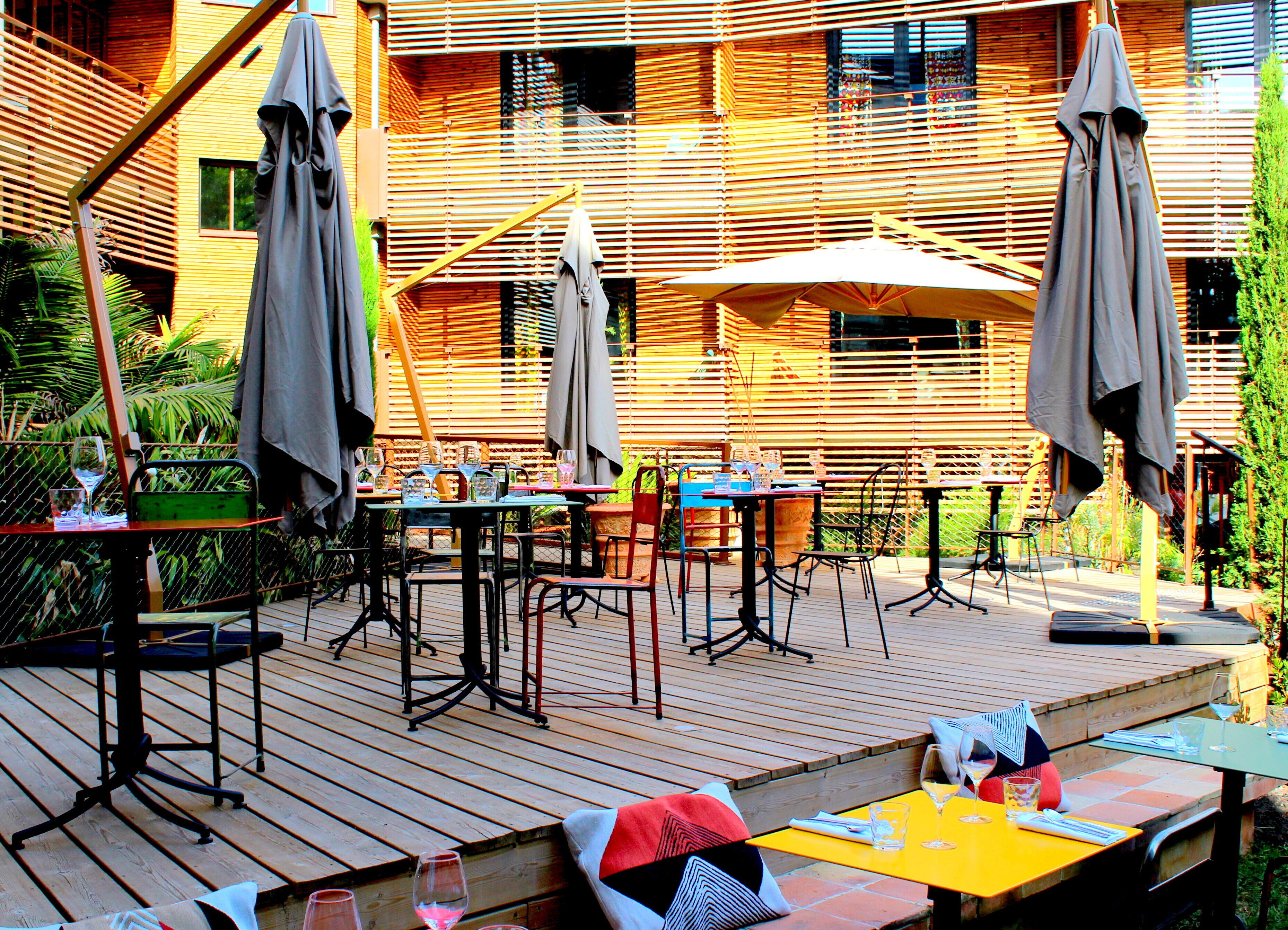 Un patio al aire libre con varias mesas y sillas, sombrillas y una terraza de madera.