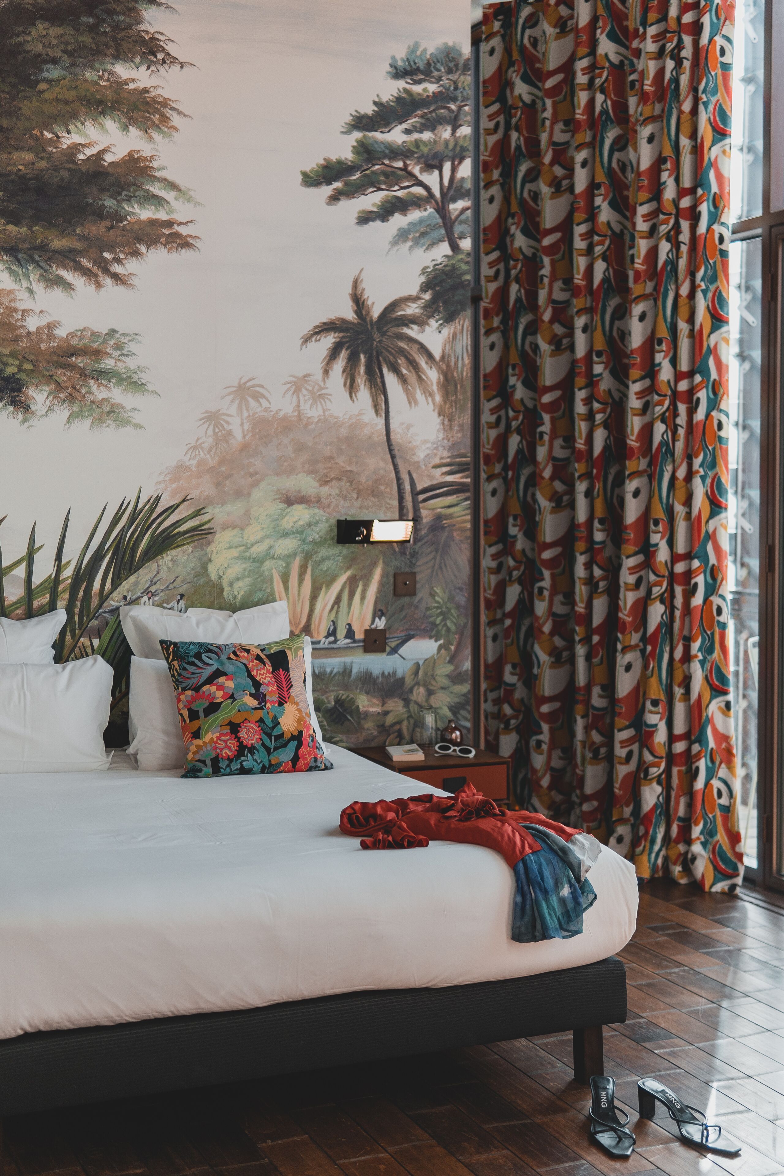 A bedroom with a bed, pillows, a nightstand, and a window with curtains.