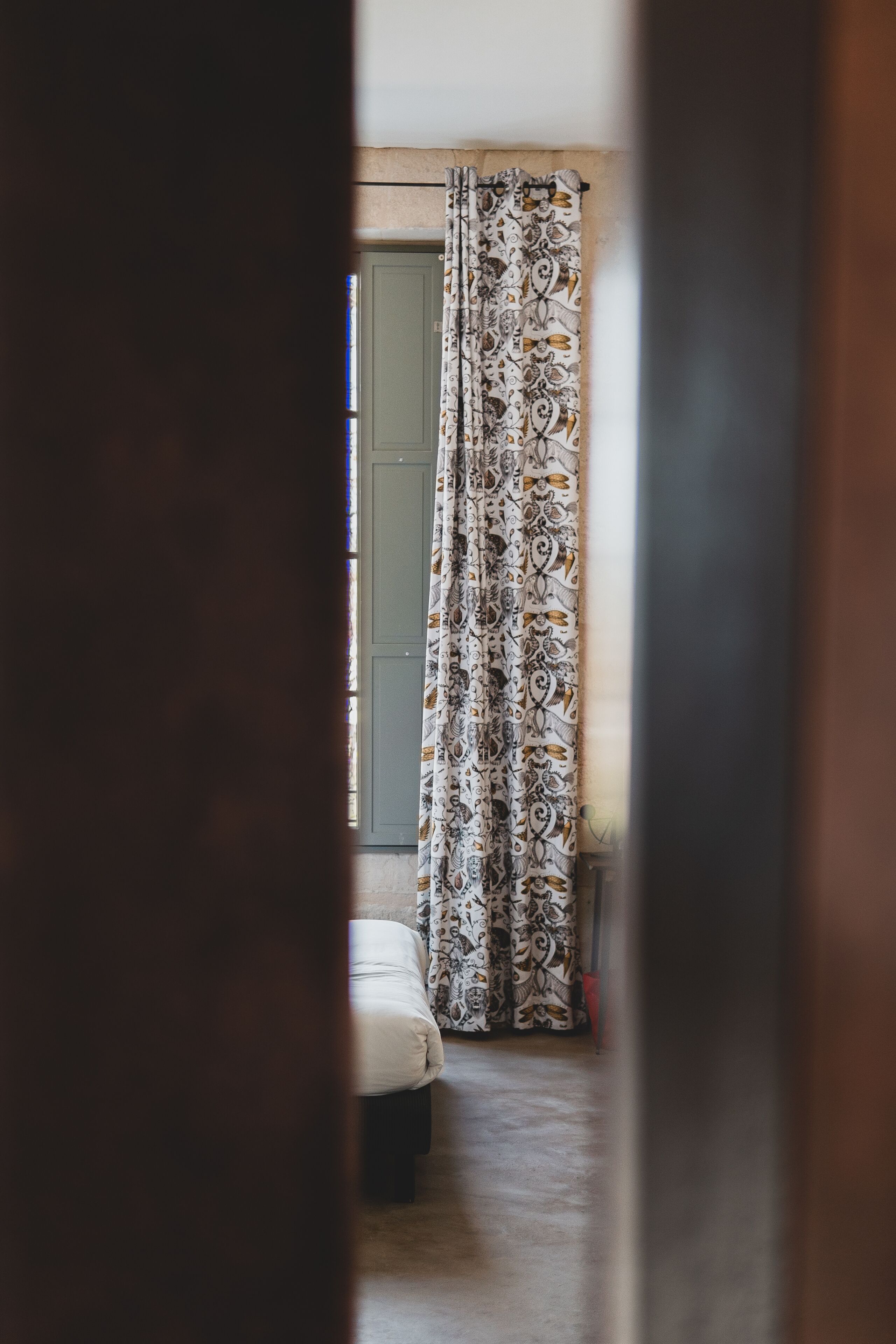 A bedroom with a patterned curtain, a bed, and a green door.