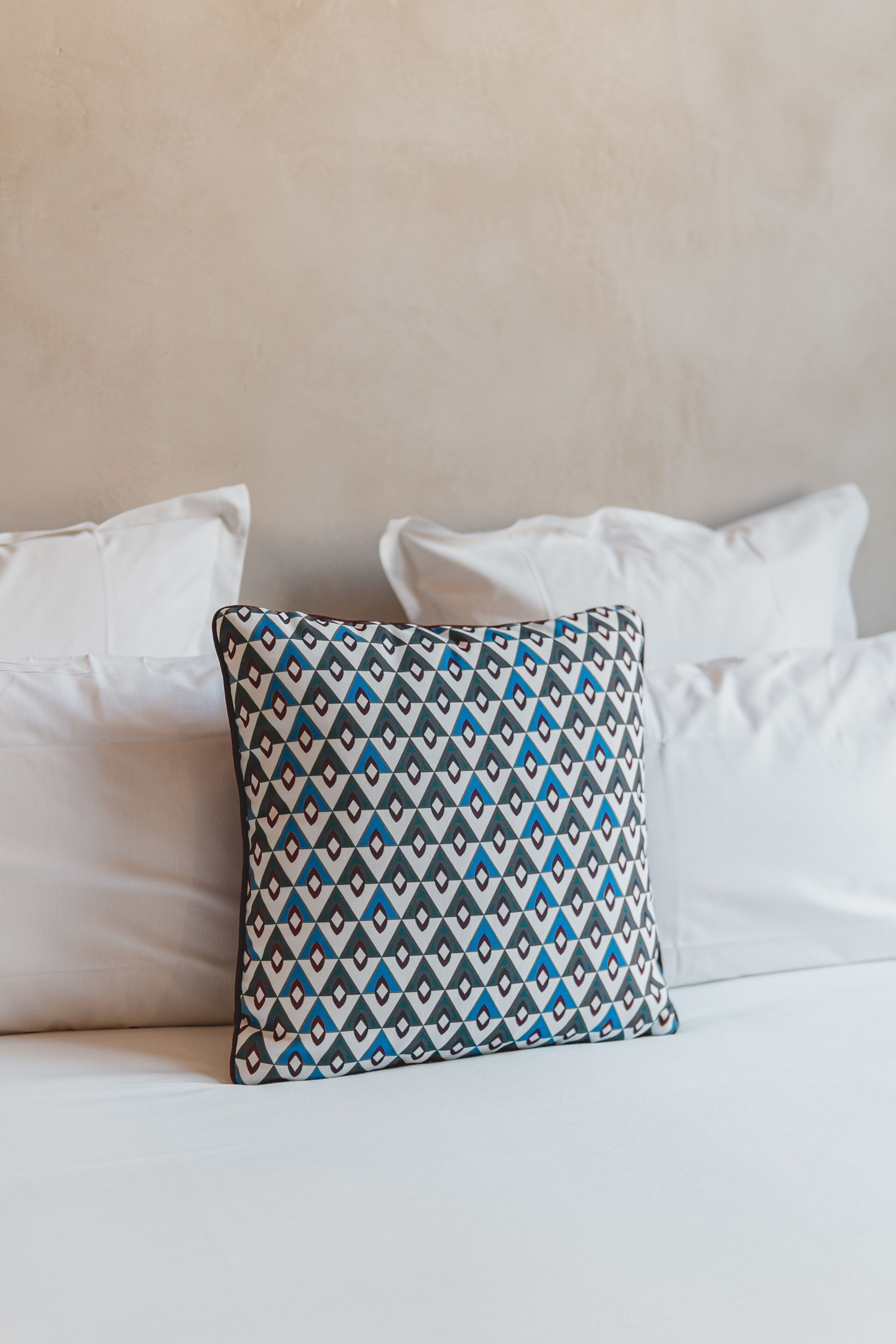 A bed with white pillows and a patterned pillow.