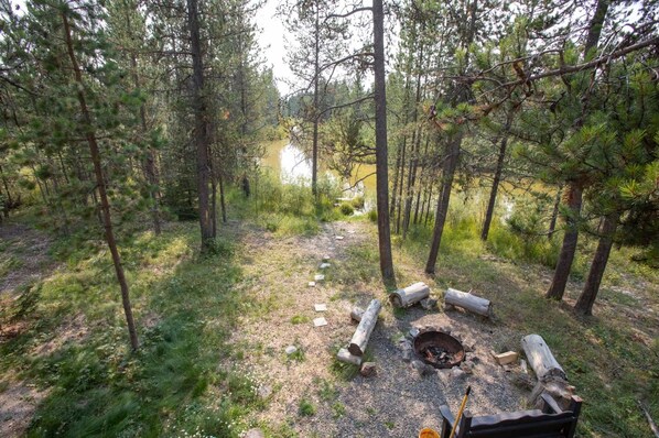 Metsäleirintäalue, jossa on nuotiopaikka, jonka ympärillä on tukkeja, ja josta on esteetön näkymä järvelle.