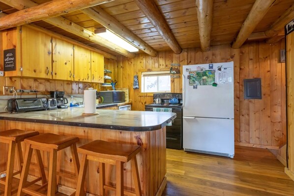 Cocina de cabaña de madera con una isla central, taburetes de bar, un refrigerador y una ventana con vistas.