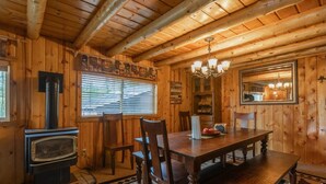 A wooden cabin interior with a dining table, chairs, a fireplace, and a chandelier.