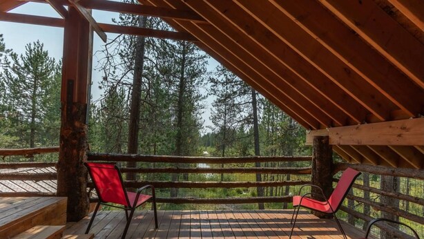 A wooden deck with red chairs and a wooden table, overlooking a forested area.