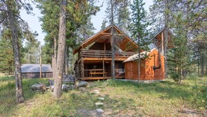 A rustic cabin with a wooden exterior, a covered porch, and a separate wooden structure to the right.