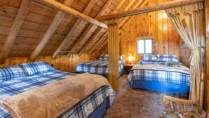 A cozy attic bedroom with wooden beams, two beds with plaid bedding, and a window providing natural light.