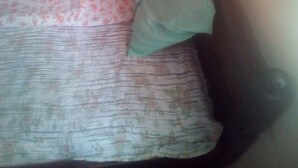 A small, dimly lit room with a single bed, a floral bedspread, and a green pillow. - Sokoni Guest House (Nairobi)