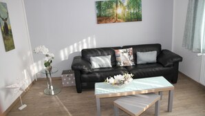 A modern living room with a black leather sofa, a glass coffee table, and a painting of a forest. - Apartment Julius 7 - beautiful, quiet and right in the middle - (St. Andreasberg)
