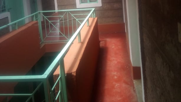 A corridor with a red floor, a green railing, and a window with green frames. - Diamond Guest House (Nairobi)