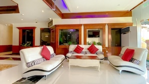 A modern living room with two white sofas with red and black striped cushions, a wooden coffee table, and large windows with a view of the outside. - New Penninsula Hotel (Dubai)