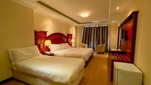 A hotel room with two beds, a desk, a chair, a TV, and a minibar. - New Penninsula Hotel (Dubai)