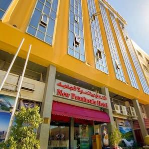 A hotel with a yellow facade, large windows, and a red awning. - New Penninsula Hotel (Dubai)