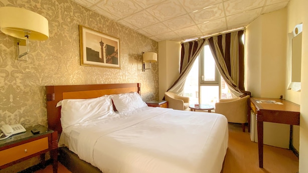 A hotel room with a large bed, a desk, a chair, a lamp, a telephone, and a window with curtains. - New Penninsula Hotel (Dubai)