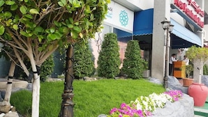 A hotel entrance with a well-maintained lawn, potted plants, and a clear view of the building's signage. - New Penninsula Hotel (Dubai)