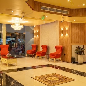 A lobby with a marble floor, red chairs, a chandelier, and a wooden wall with lighting. - New Penninsula Hotel (Dubai)