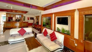 A reception area with a wooden reception desk, two white sofas with red cushions, a large flat-screen TV, and a decorative ceiling light. - New Penninsula Hotel (Dubai)