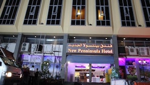The exterior of the New Penninsula Hotel with a clear sign, large windows, and a well-lit entrance. - New Penninsula Hotel (Dubai)
