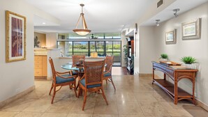 A dining area with a round table and chairs, a hanging light fixture, and a view through the glass door. - Beautiful updates--everything new! Golf course views!  Huge 2/2 K. Royal #A301 (Lahaina)