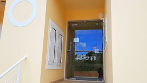 A building entrance with a glass door, a white handrail, and a circular sign on the wall. - Superb 2-bedroom Luz Apt has AC, Wi Fi, Pool, near restaurants & beach! (Luz-Lagos)