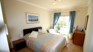 A bedroom with a bed, bedside table, lamp, and a window with curtains. - Superb 2-bedroom Luz Apt has AC, Wi Fi, Pool, near restaurants & beach! (Luz-Lagos)