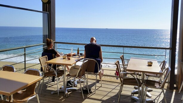 A deck with tables and chairs overlooking the ocean. - Superb 2-bedroom Luz Apt has AC, Wi Fi, Pool, near restaurants & beach! (Luz-Lagos)