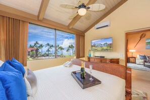 A hotel room with a large bed, a TV, and a view of palm trees and a beach.