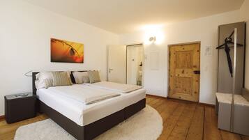 A bedroom with a bed, a nightstand, a painting, a door, and a coat rack.