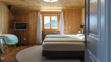 A wooden-paneled room with a bed, a television, a chair, and a window with curtains.