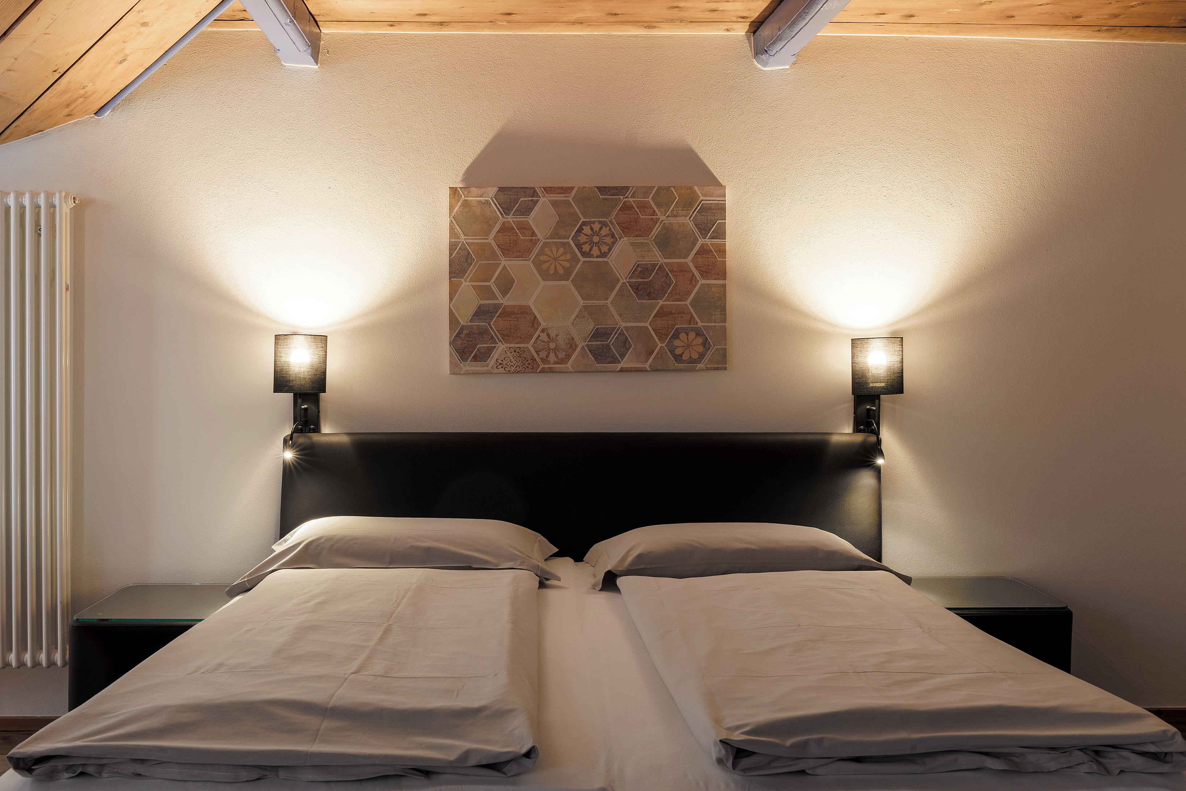 Une chambre à coucher comprenant un lit, deux tables de chevet, un luminaire fixé au mur et un radiateur.
