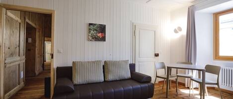 Una sala de estar moderna con un sofá de cuero oscuro, una mesa de comedor con sillas y un cuadro en la pared.